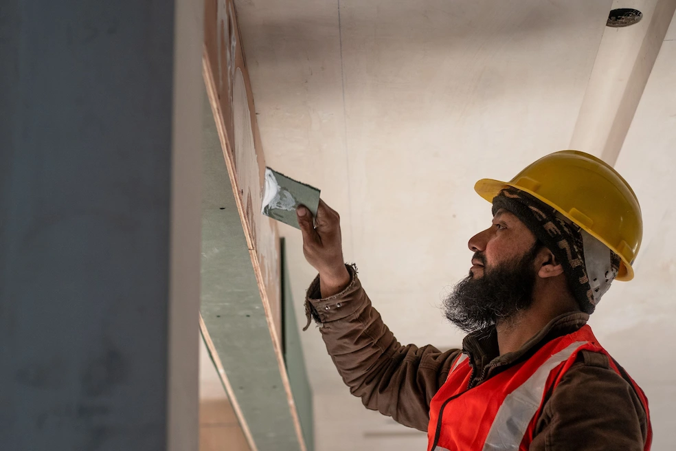 Worker wearing a hard hat and smoothing an interior wall, image for Los Angeles Stucco Build & Repair.